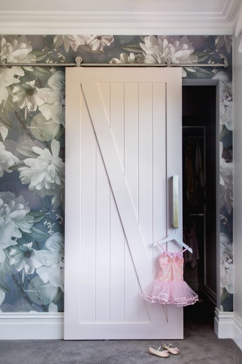 Floral wallpaper and pink barn door in a girl's bedroom.