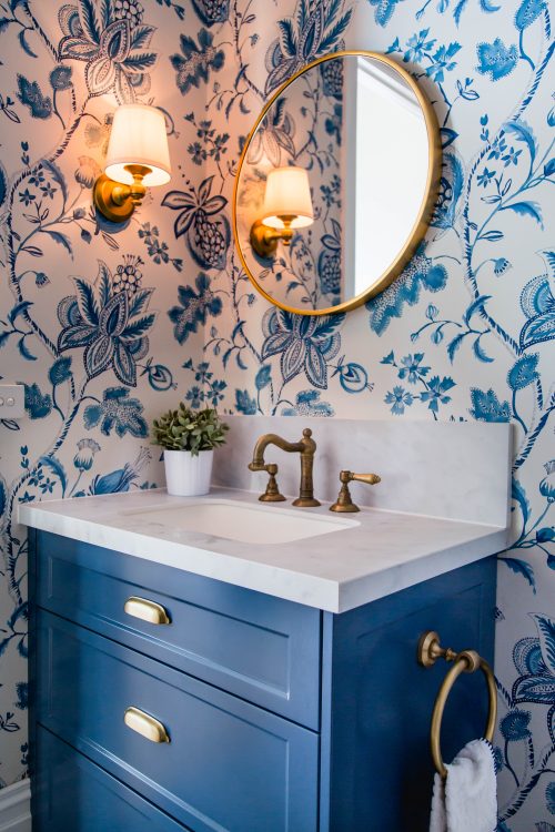 A Hamptons inspired powder room with blue floral wallpaper and brass accents.